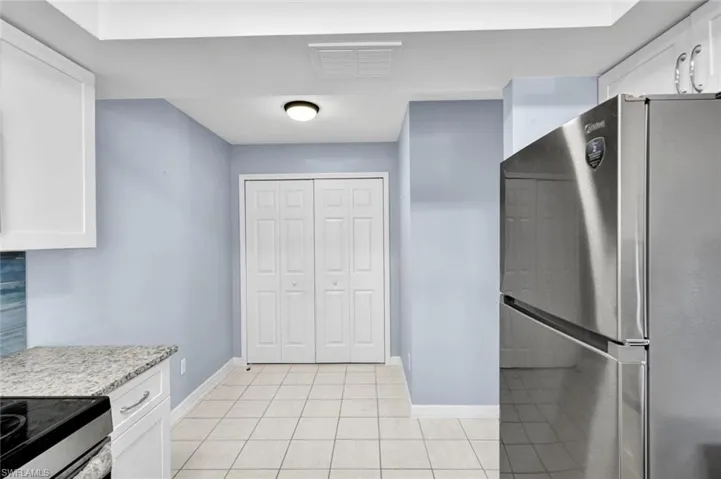 Kitchen featuring freestanding refrigerator, white cabinets, light stone countertops, range with electric cooktop, and light tile patterned floors