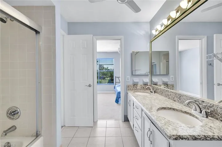Ensuite bathroom featuring double vanity, a ceiling fan, light tile patterned flooring, and combined bath / shower with glass door