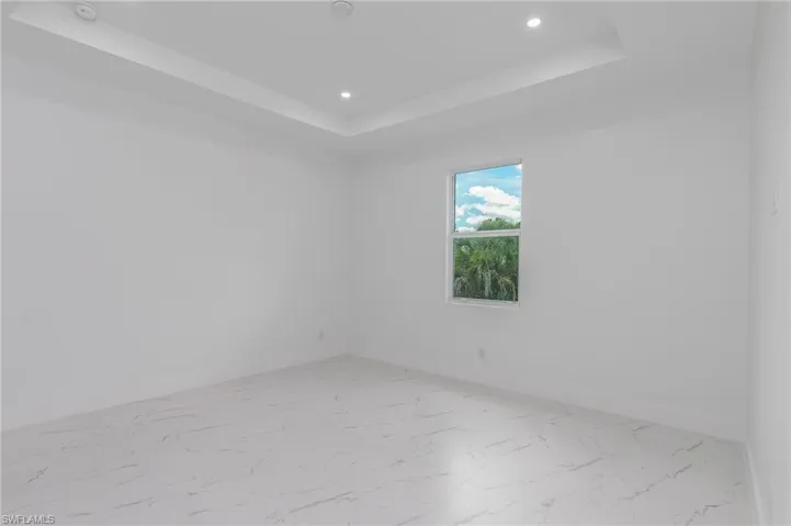 Spacious interior featuring a single window, tray ceiling with recessed lighting, and large format tile flooring