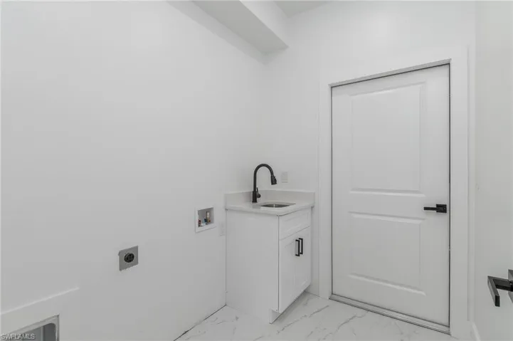 Utility area featuring a white shaker-style vanity with a single basin sink, matte black faucet, and stone countertop