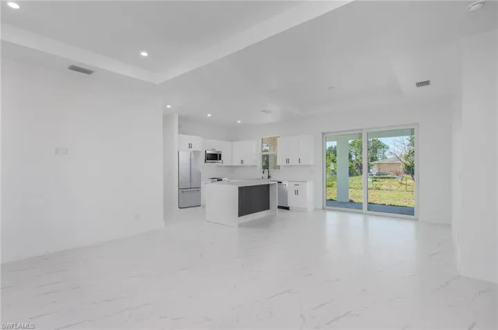 Open-concept kitchen and living area featuring white cabinetry, stainless steel appliances, a center island with a dark accent panel, and recessed lighting