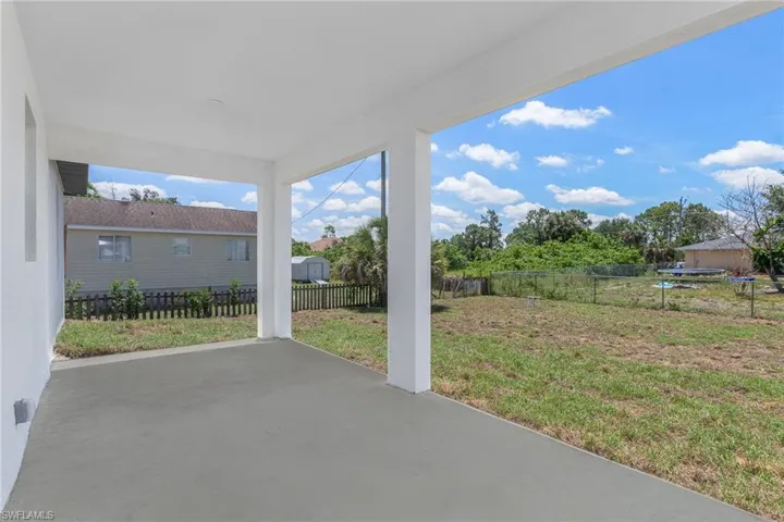 Covered patio with a smooth concrete surface, supported by white columns, opening to a spacious grassy yard