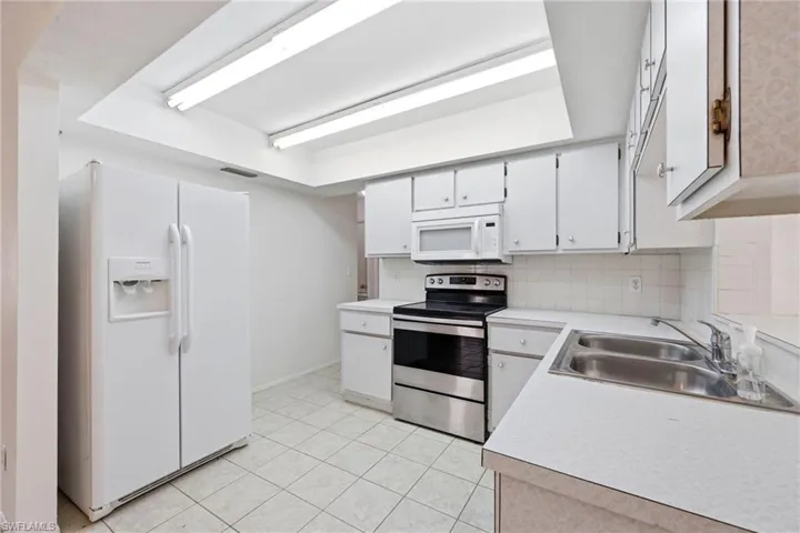 Kitchen featuring white appliances, light countertops, white cabinets, tasteful backsplash, and light tile patterned floors