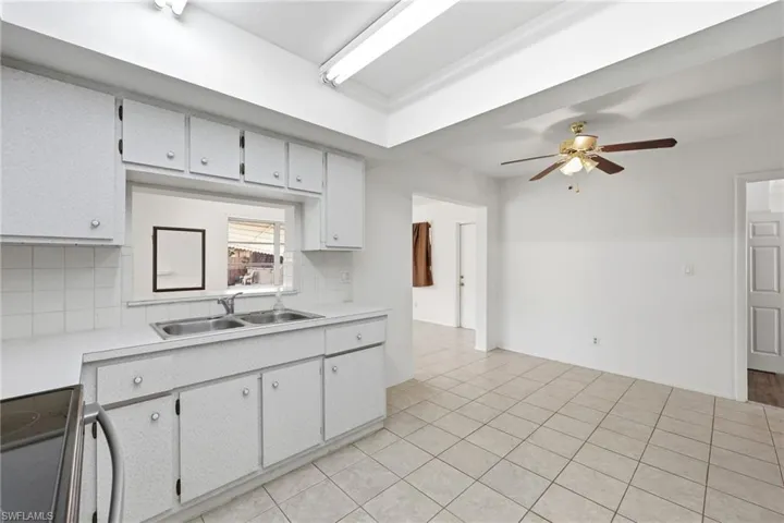 Kitchen with light countertops, black range with electric cooktop, decorative backsplash, ceiling fan, and light tile patterned floors