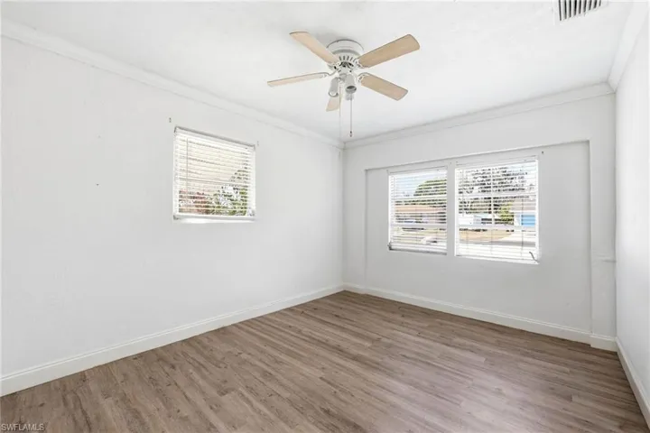 Empty room with wood finished floors, a ceiling fan, plenty of natural light, and crown molding