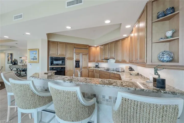 Kitchen with paneled built in refrigerator, kitchen peninsula, black oven, and light stone counters