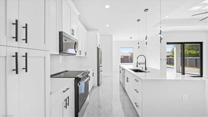 Kitchen with stainless steel appliances, a large island, hanging light fixtures, white cabinets, and light stone counters