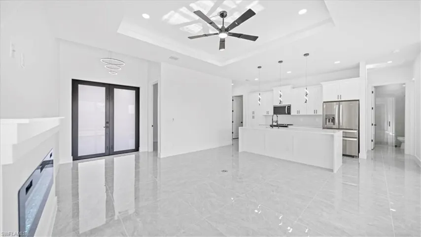 Unfurnished living room featuring french doors, a ceiling fan, recessed lighting, and a raised ceiling
