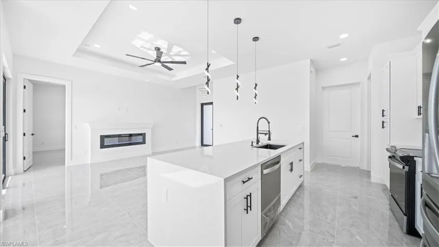 Kitchen with hanging light fixtures, light stone countertops, white cabinetry, a glass covered fireplace, and ceiling fan