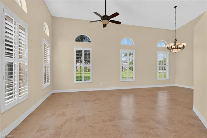 Vaulted ceilings featuring a multi-light chandelier and ceiling fan, large windows with arched transoms, and plantation shutters over tile flooring
