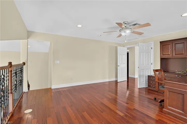 Wood-finish flooring, wrought iron staircase railing, recessed lighting, ceiling fan, and built-in dark wood cabinetry