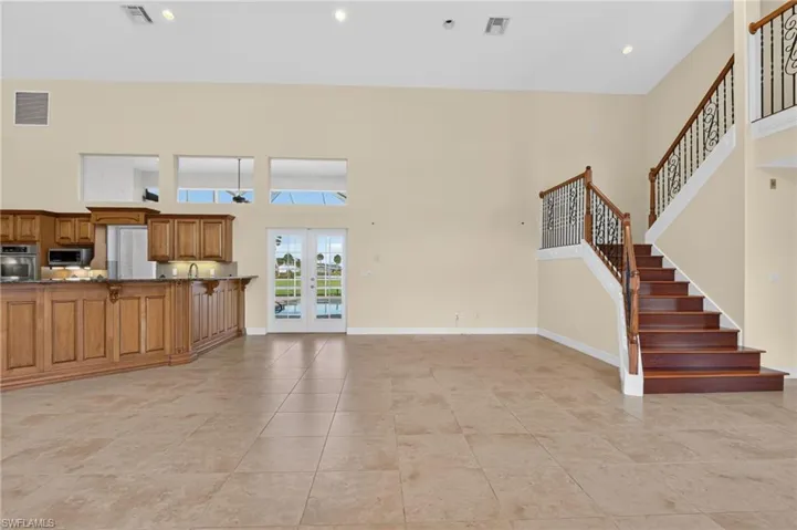 Open floor plan featuring high ceilings, stone-finish tile flooring, custom wood cabinetry, and a staircase with decorative iron railings