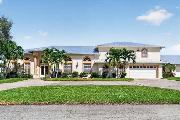 Stucco exterior featuring arched windows, metal roofing, an attached garage, and a covered entryway with structural columns