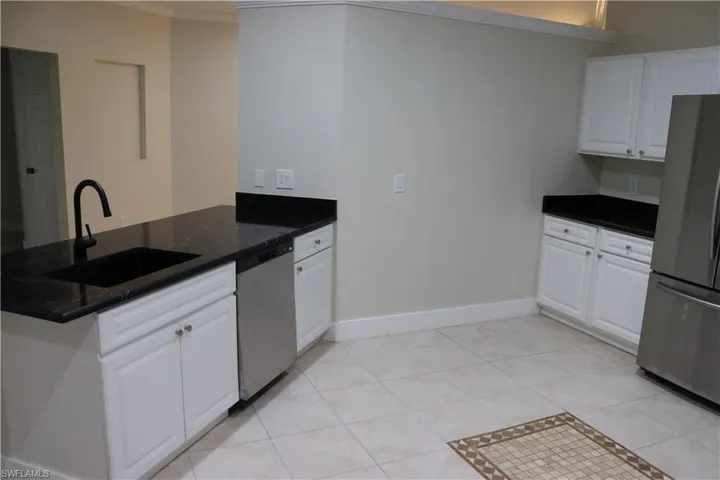 Kitchen with appliances with stainless steel finishes, white cabinets, light tile patterned flooring, a peninsula, and crown molding