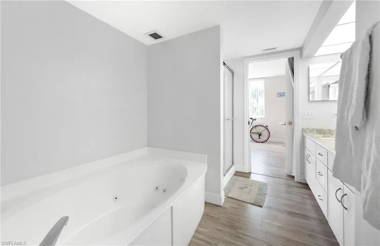 Full bath with a jetted tub, light wood-style flooring, vanity, and a shower stall