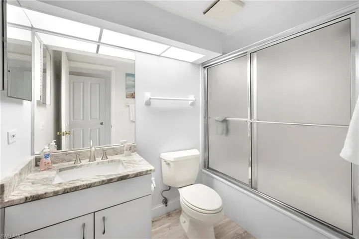 Bathroom featuring combined bath / shower with glass door, vanity, and light wood-style flooring