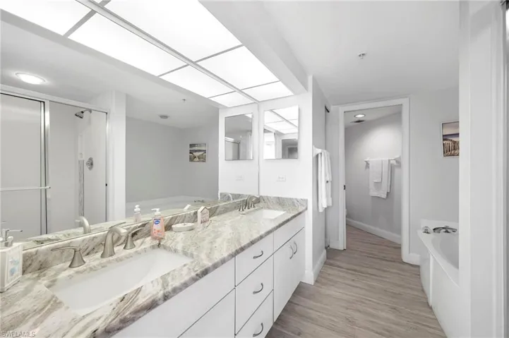 Bathroom with a bath, double vanity, a stall shower, and light wood finished floors