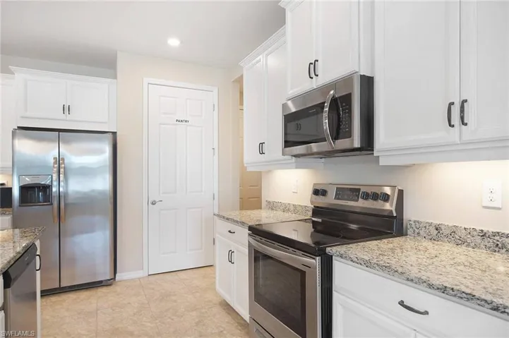 Kitchen with stainless steel appliances, white cabinetry, light stone countertops, recessed lighting, and light tile flooring