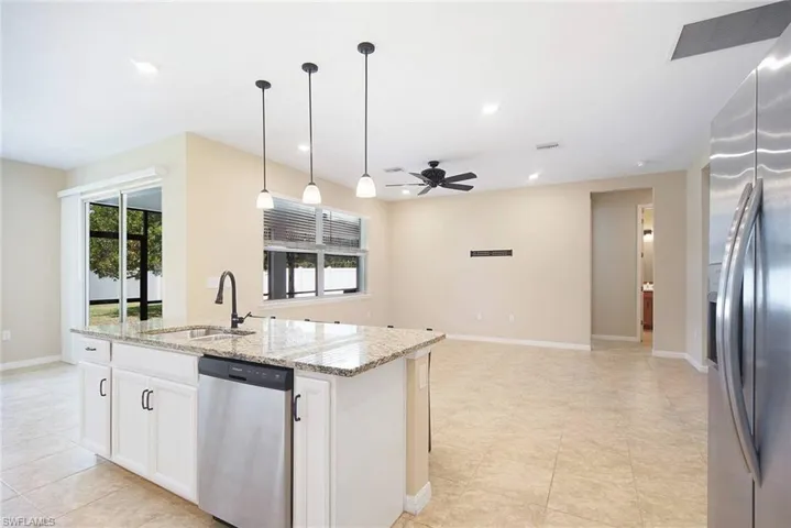 Kitchen with stainless steel appliances, light stone countertops, open floor plan, white cabinets, and pendant lighting