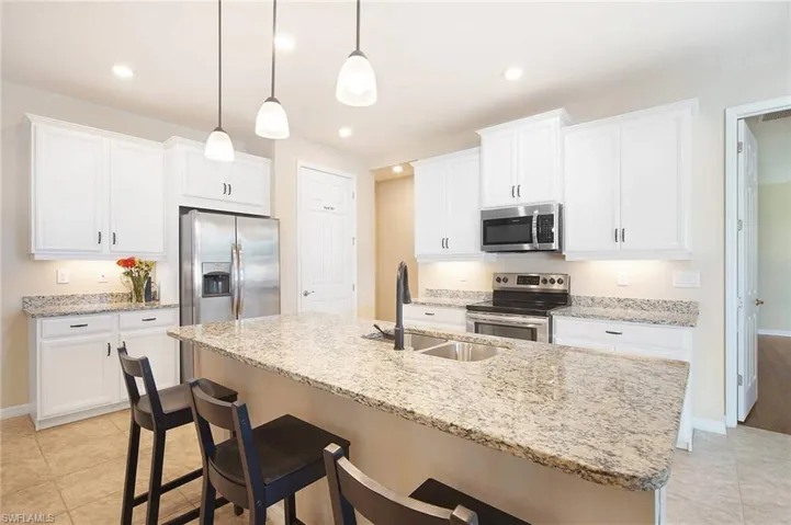 Kitchen featuring light tile floors, a kitchen breakfast bar, stainless steel appliances, and light stone counters
