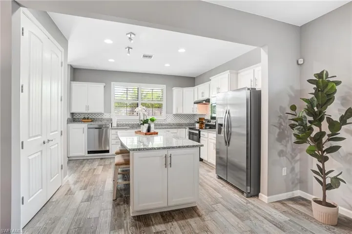 Kitchen with appliances with stainless steel finishes, tasteful backsplash, under cabinet range hood, light wood finished floors, and recessed lighting