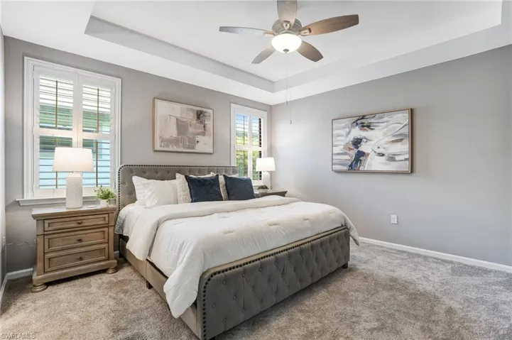 Bedroom featuring light carpet, a raised ceiling, baseboards, and ceiling fan