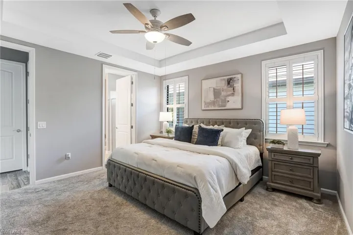 Carpeted bedroom featuring a tray ceiling, baseboards, connected bathroom, and ceiling fan