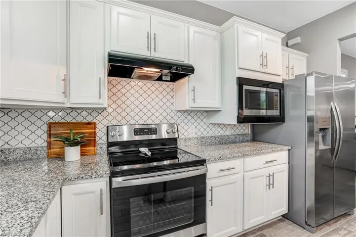 Kitchen featuring stainless steel appliances, under cabinet range hood, white cabinets, and tasteful backsplash