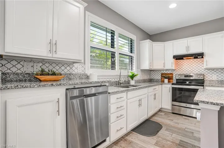 Kitchen with appliances with stainless steel finishes, a sink, under cabinet range hood, white cabinetry, and light wood-type flooring