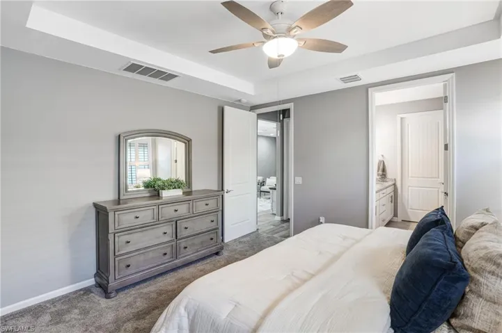 Bedroom featuring dark carpet, a raised ceiling, baseboards, ceiling fan, and connected bathroom