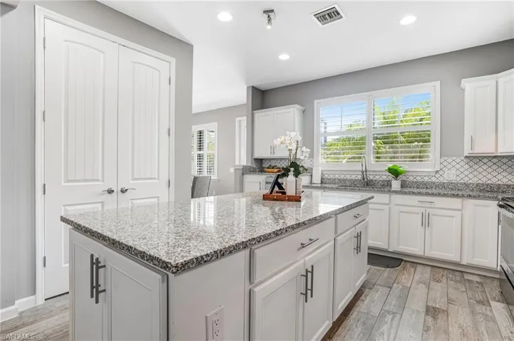 Kitchen with a sink, light wood-style flooring, a kitchen island, backsplash, and white cabinetry