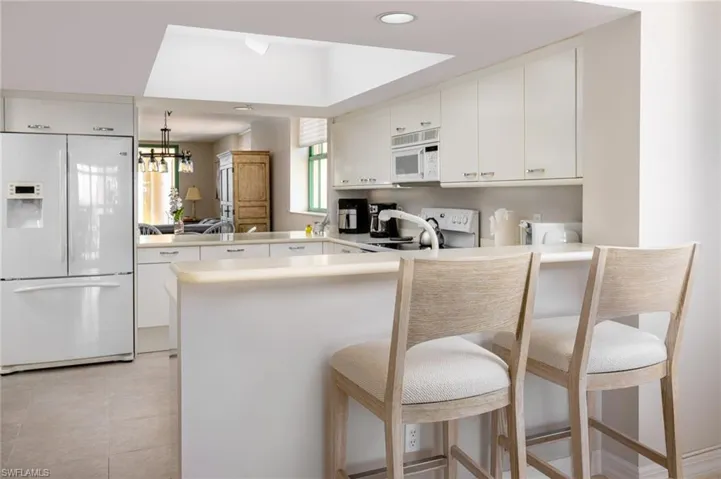 Kitchen with white appliances, a peninsula, light countertops, and a kitchen breakfast bar