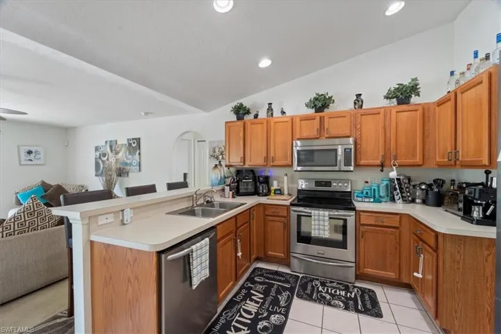 Kitchen with sink, kitchen peninsula, vaulted ceiling, light tile patterned floors, and appliances with stainless steel finishes