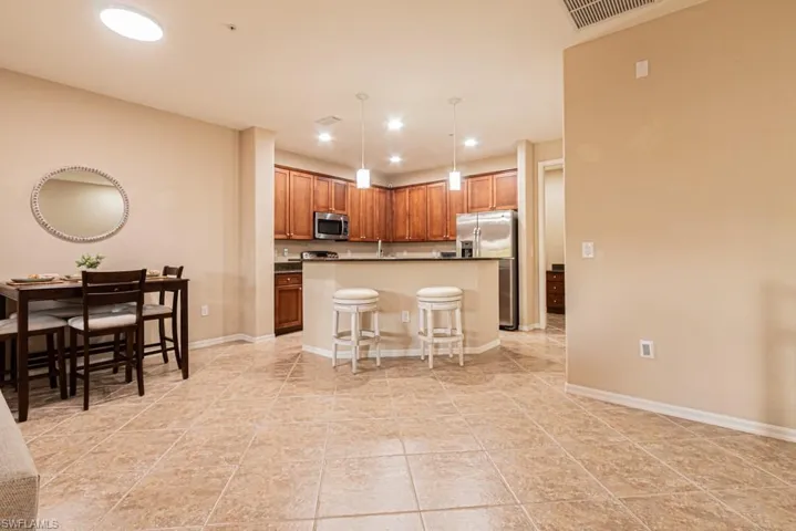 Kitchen featuring light tile patterned flooring, decorative light fixtures, a center island, appliances with stainless steel finishes, and a kitchen breakfast bar
