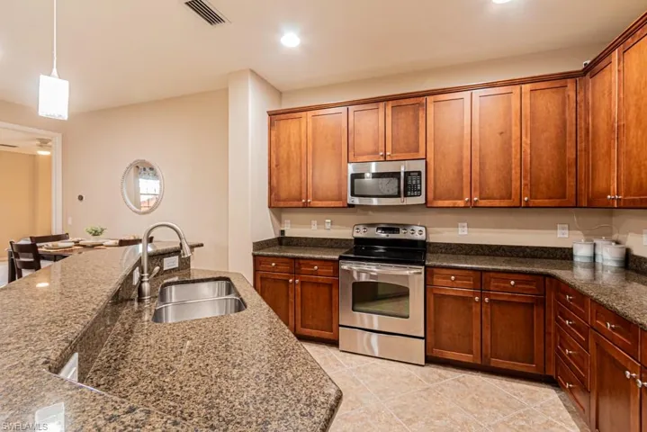 Kitchen featuring dark stone counters, decorative light fixtures, sink, appliances with stainless steel finishes, and light tile patterned floors