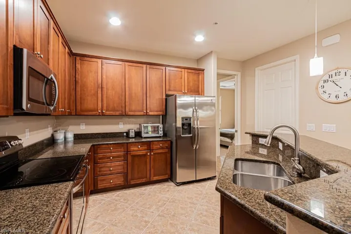 Kitchen featuring appliances with stainless steel finishes, sink, hanging light fixtures, light tile patterned floors, and dark stone countertops