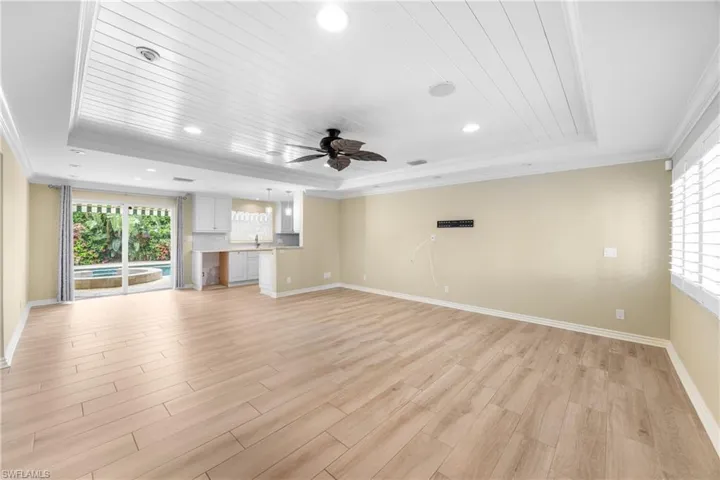 Unfurnished living room with a tray ceiling, crown molding, healthy amount of natural light, light wood-style floors, and recessed lighting