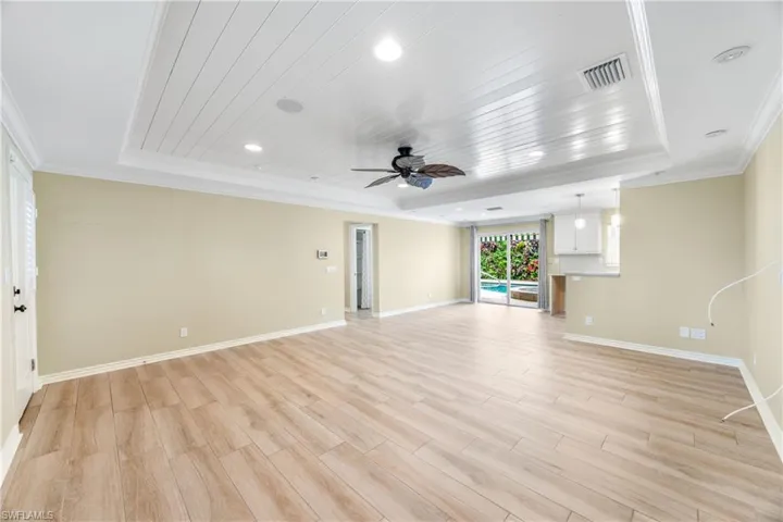 Unfurnished living room with a raised ceiling, ceiling fan, ornamental molding, light wood-style flooring, and recessed lighting