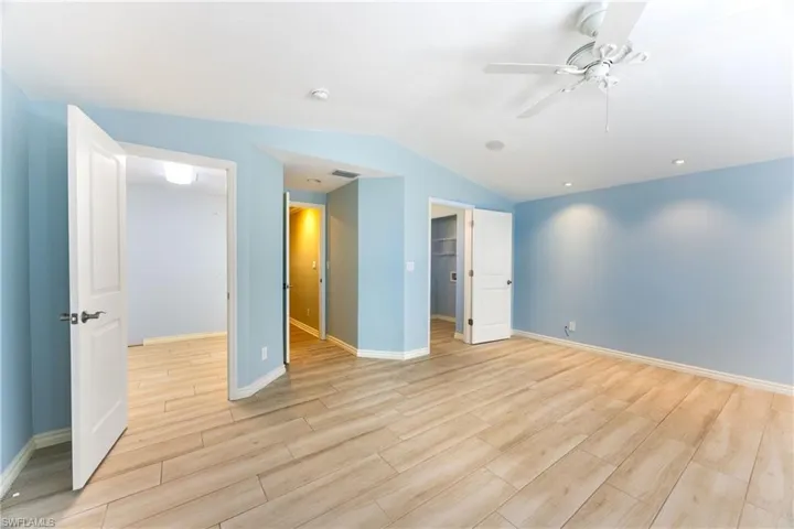 Unfurnished bedroom with light wood-style floors, vaulted ceiling, a spacious closet, and ceiling fan