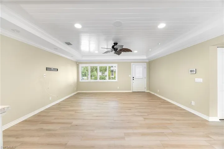 Empty room featuring ceiling fan, crown molding, light wood-style flooring, recessed lighting, and a tray ceiling