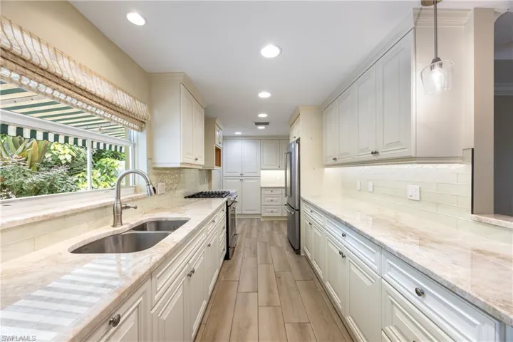 Kitchen featuring stainless steel appliances, light stone counters, light wood-style floors, recessed lighting, and decorative backsplash