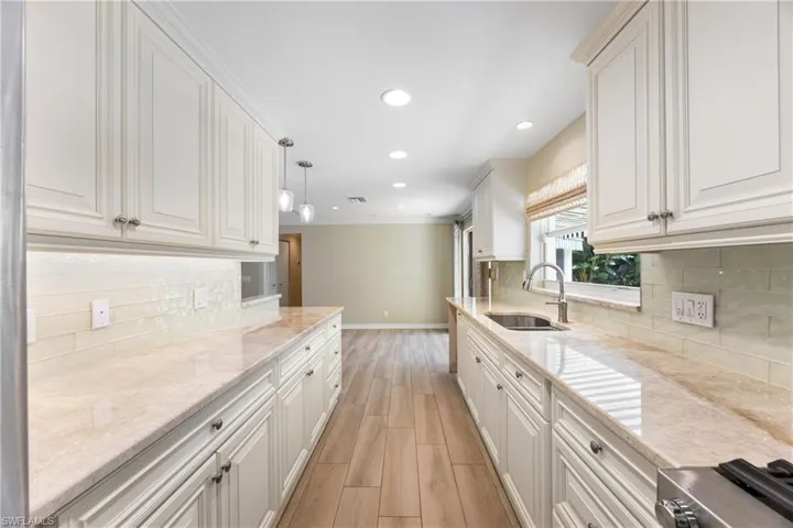 Kitchen featuring light wood finished floors, recessed lighting, tasteful backsplash, white cabinetry, and light stone countertops