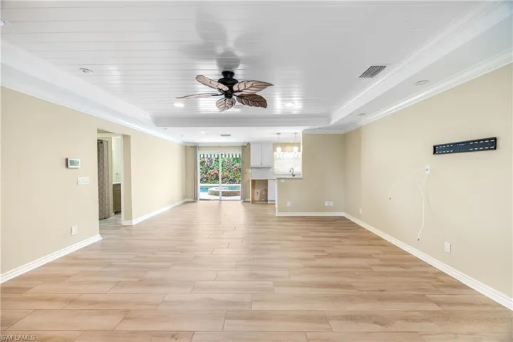 Unfurnished living room with ceiling fan, ornamental molding, light wood-type flooring, and a tray ceiling