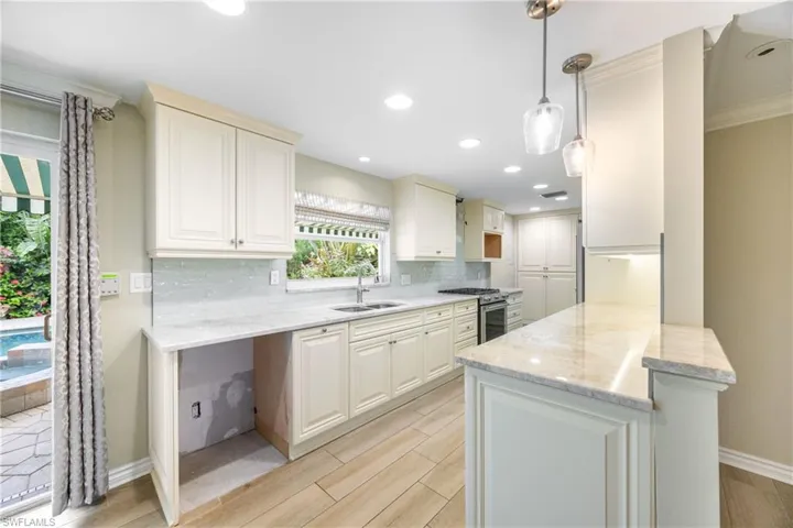 Kitchen featuring gas range, decorative backsplash, light stone counters, a peninsula, and wood tiled floors