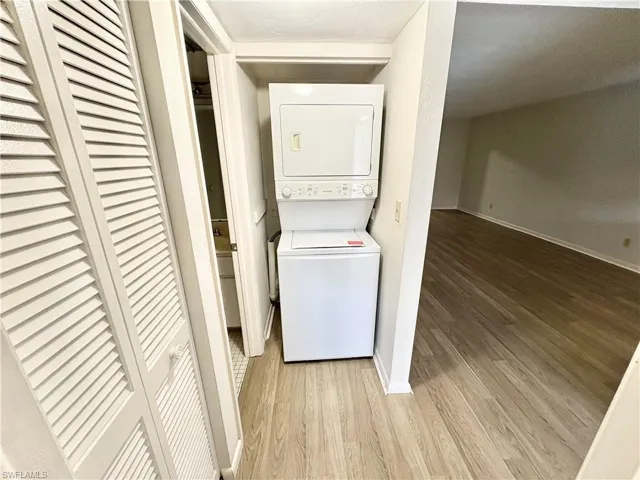 Laundry room with stacked washer / dryer, light wood-style flooring, and baseboards