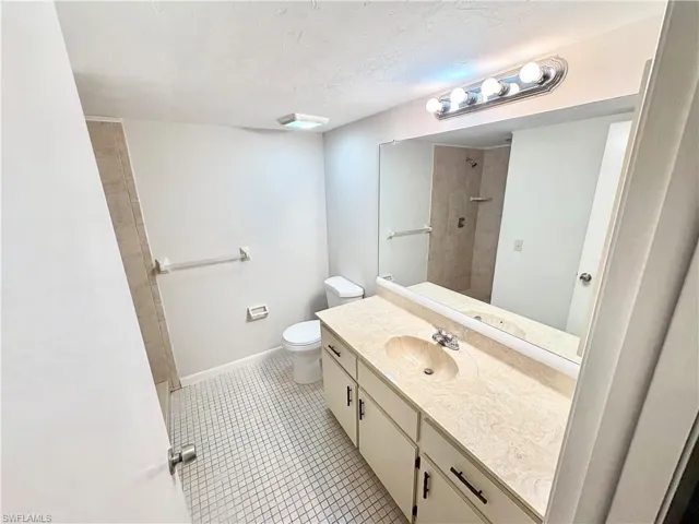 Full bath with vanity, toilet, a tile shower, tile patterned floors, and baseboards