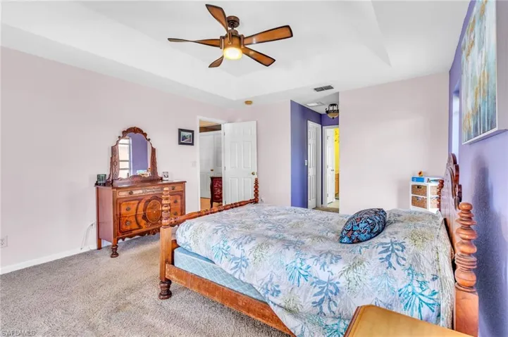 Bedroom with carpet flooring, a tray ceiling, visible vents, baseboards, and a ceiling fan