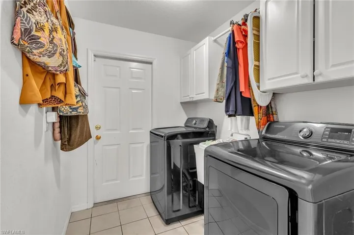 Washroom with washing machine and dryer, baseboards, light tile patterned flooring, and cabinet space