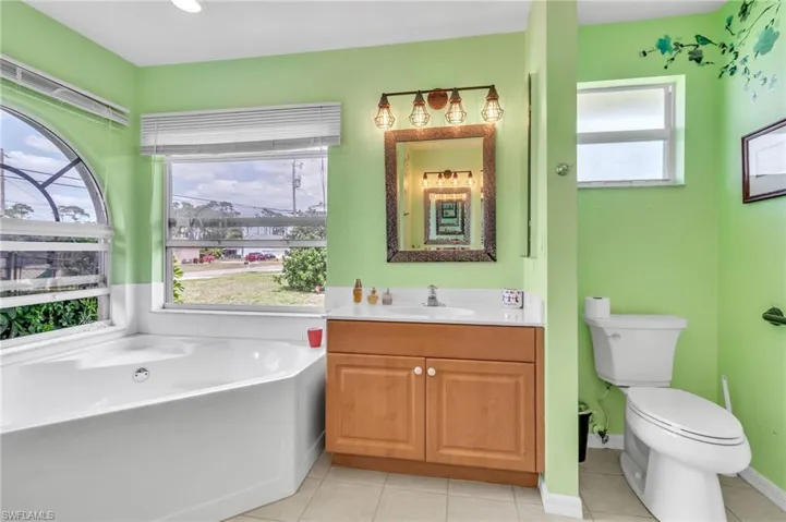Bathroom featuring a garden tub, vanity, tile patterned flooring, and toilet