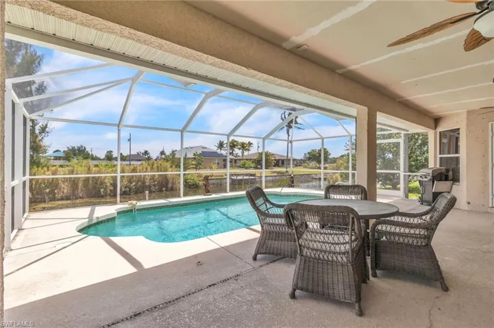Outdoor pool with grilling area, a ceiling fan, glass enclosure, and a patio